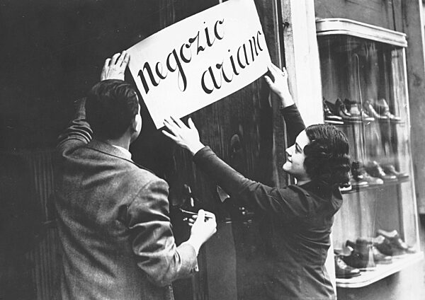Italian proprietors placing an anti-semitic sign outside their shoe shop, Italy, 18th December 1938 (b/w photo)