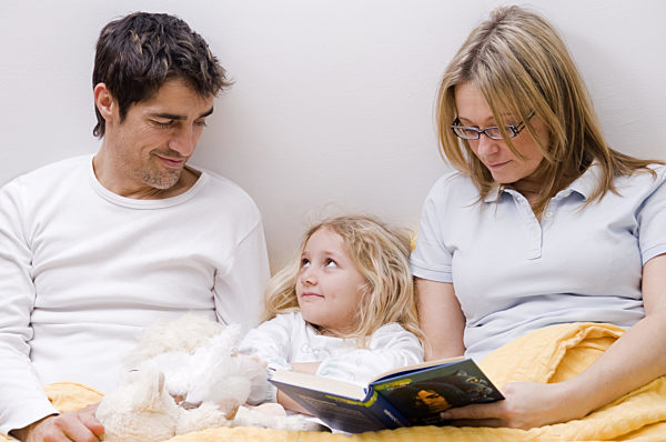 Eltern und Tochter gemeinsam im Bett, Mutter liest aus einem Buch vor, parents and daughter together in a bed