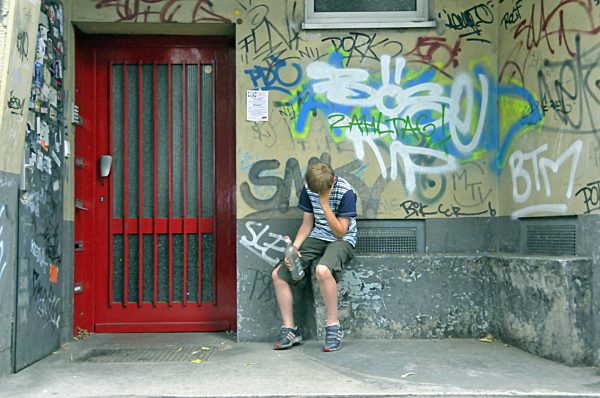 frustierter neunjaehriger Junge mit Alkoholflasche in einem verschmierten Hauseingang, Deutschland, Europa, drunken teenager with alcohol bottle in front of a house entrance with graffitis