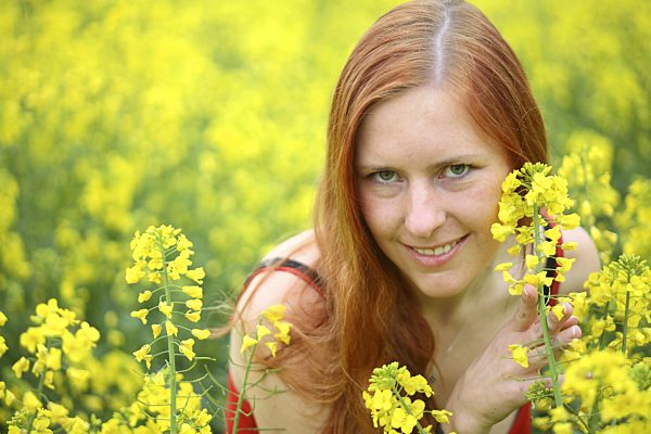 huebsche junge Frau mit langem rotem Haar im Rapsfeld, young attractive woman with red hair in a rape field