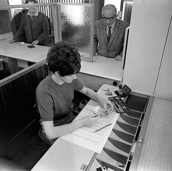 Eine Angestellte zählt das Geld nach, das ein älterer Herr im Anzug am...