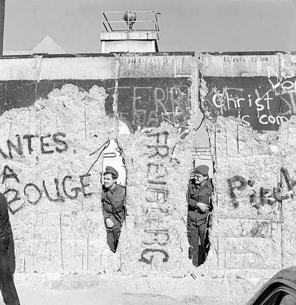 Zwei Soldaten der Grenztruppen der DDR schauen durch ein Loch in der Berliner Mauer in Berlin