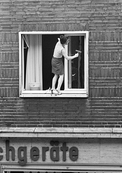 Siebziger Jahre, Menschen, Unfallgefahr, junge Frau beim Fenster putzen in Pantoletten steht im Obergeschoss eines Hauses mit einem Bein auf dem aeusseren Fenstersims und beugt sich nach aussen vor