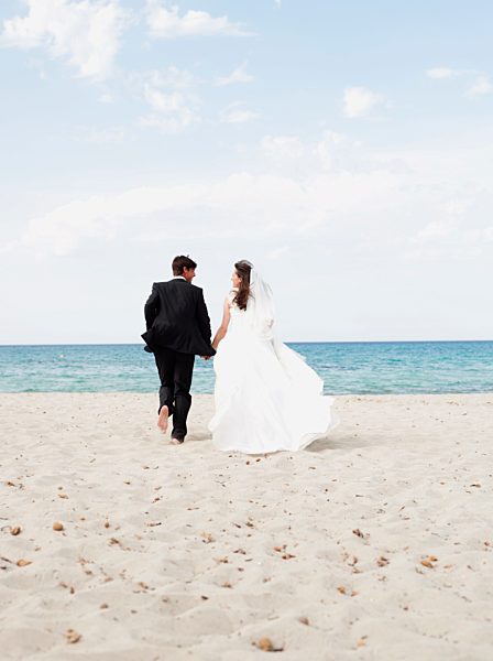 bride and groom running along beach