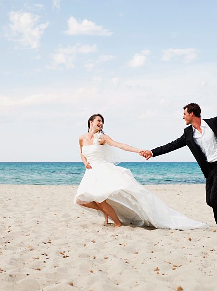 bride and groom running along beach