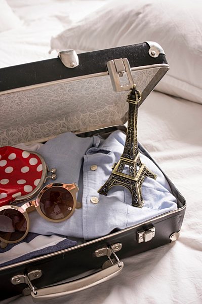 Open suitcase on bed with eiffel tower souvenir and sunglasses