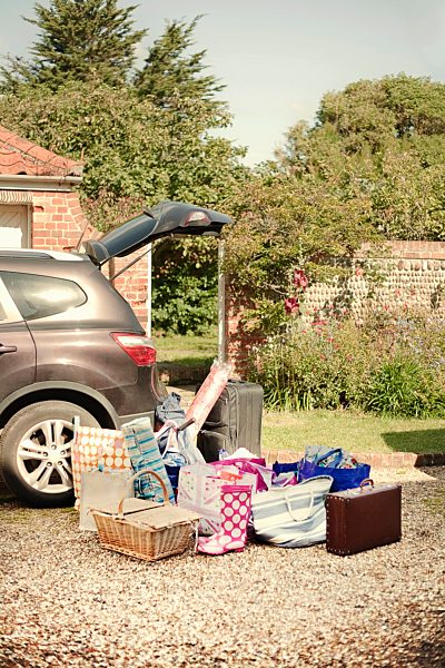 Car boot open with suitcases, baskets and bags prepared on drive