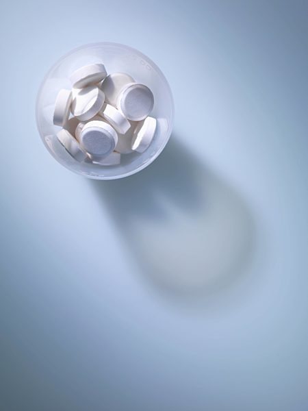 Overhead view of white tablets in plastic measuring cup