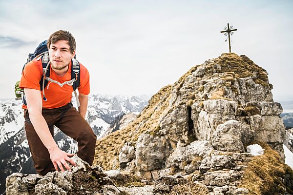 Young male hiker climbing on peak of Klammspitze mountain, Oberammergau, Bavaria, Germany