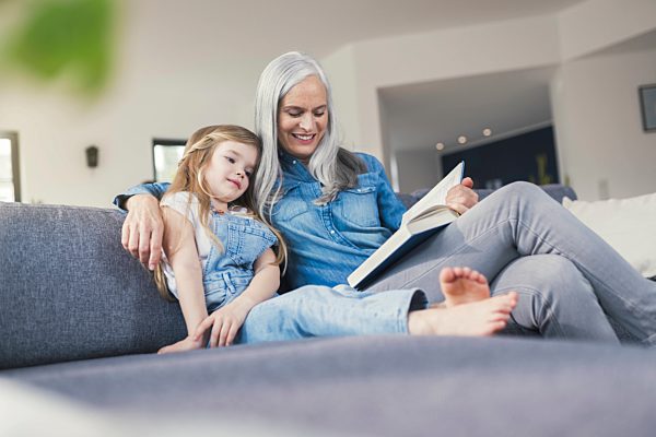 Grandmother and granddaughter sitting on couch, reading together