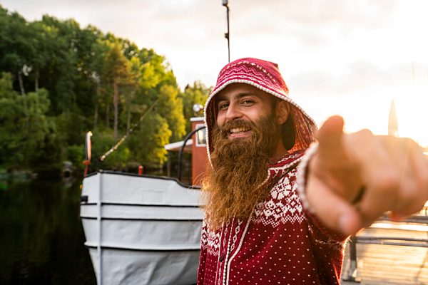 Finland, Kajaani, Cheerful young man. wearing houded jacket, standing on jetty, making hand gestures