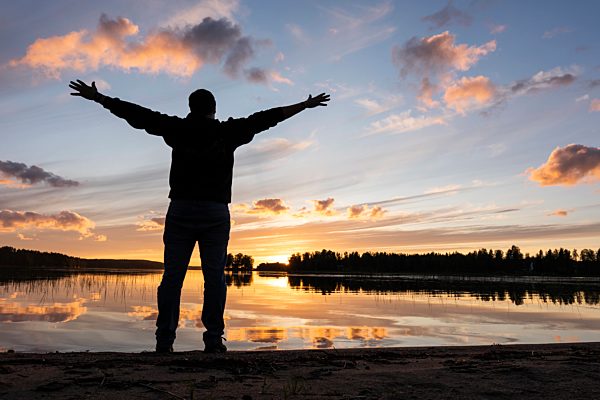 Finland, Kajaani, Man watching sunset at the river with arms outstretched
