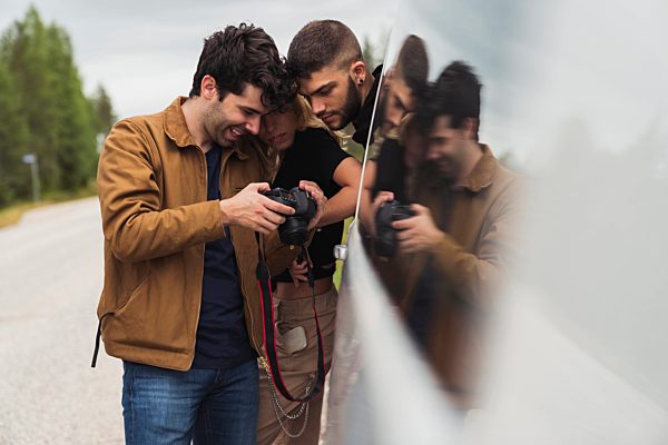 Finland, Lapland, friends checking pictures on digital camera at country road