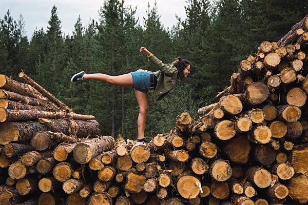 Young woman standing on one leg on stack of wood
