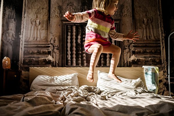 Little girl jumping on parent's bed at home