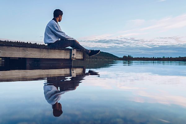 Young man sitting at lake Inari, looking at view, Finland