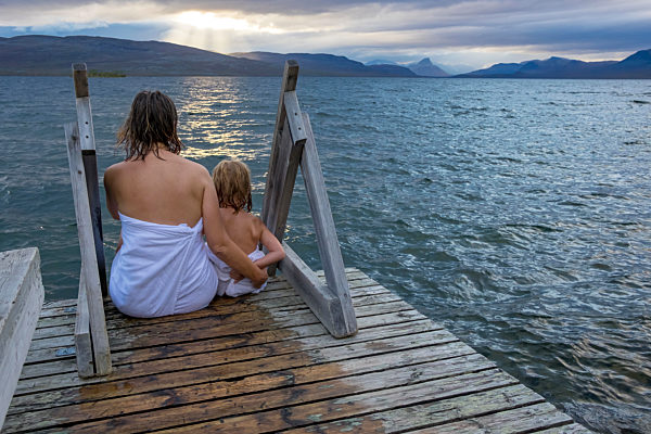 Finland, Lappland, Kilpisjaervi, mother and daughter sitting outside on boardwalk, rear view