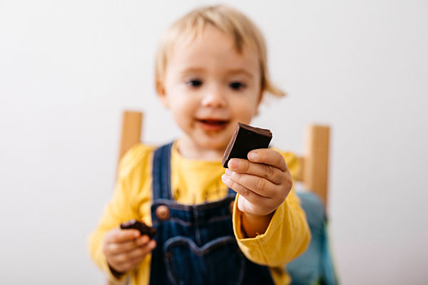 Hand of smiling toddler girl holding piece of chocolate, close-up