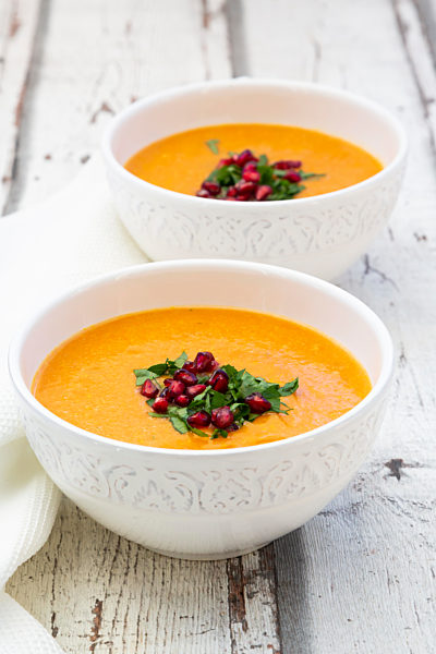 Bowls of carrot ginger coconut soup with topping of parsley and pomegranate seed