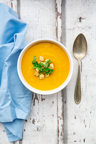 Bowl of sweet potato soup with mango, curcuma and coconut milk, croutons and basil