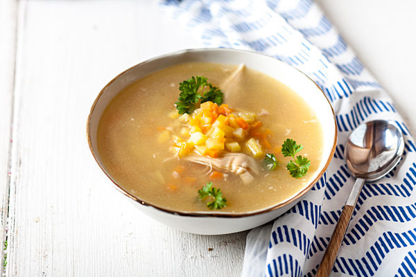 Bowl of homemade chicken stock with potatoes, carrots and parsley
