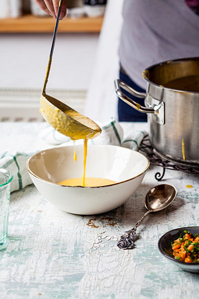 Woman pouring creme of carrot soup into a bowl, partial view