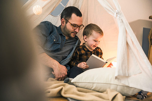 Father and son reading a book together in tent at home