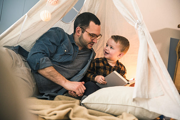Father and son reading a book together in tent at home