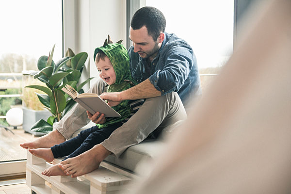 Boy in a costume with father reading book at home