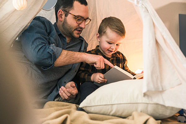 Father and son reading a book together in tent at home