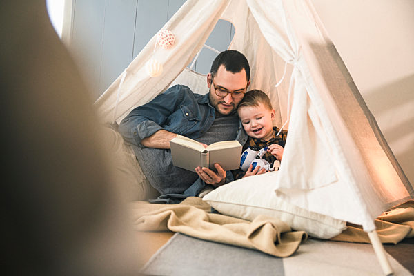 Father and son reading a book together in tent at home
