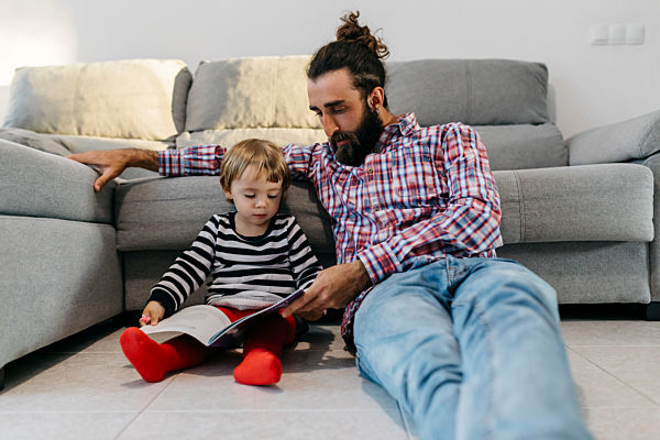 Father and little daughter sitting in the floor in the living room reading a book together