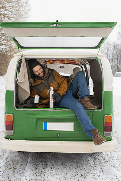 Happy man with electric van in winter landscape having a break, Kuopio, Finland