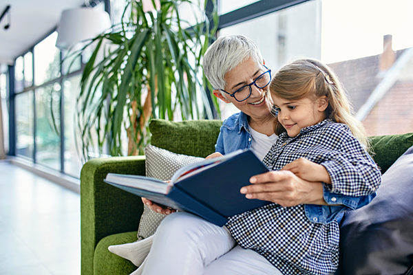 Grandmother sitting on couch with granddaughter, reading book together