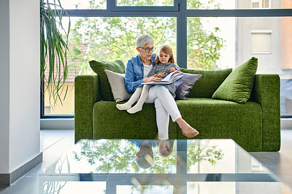 Grandmother sitting on couch with granddaughter, reading book together
