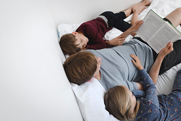 Father reading book with daughter and son in bed