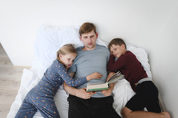 Father reading book with daughter and son in bed