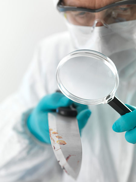 Forensic scientist examining a knife taken from a violent crime scene in the laboratory