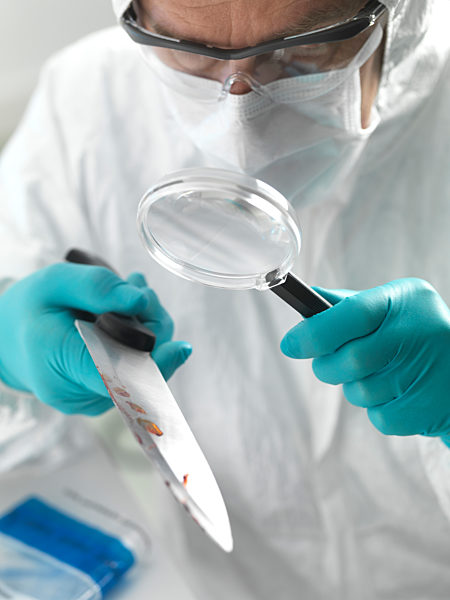 Forensic scientist examining a knife taken from a violent crime scene in the laboratory