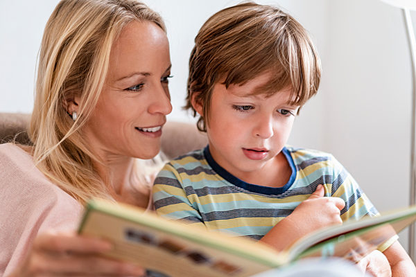 Mother and son reading a book together on couch at home