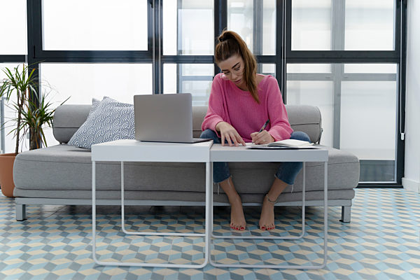 Young woman sitting on the couch writing in notebook