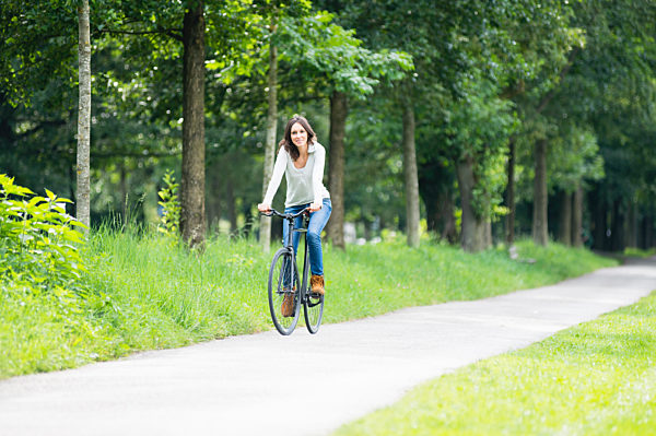 Smiling woman riding bicycle on footpath against green trees at park