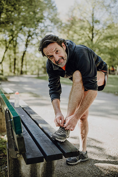 Smiling mature man tying shoelace on bench while standing in park