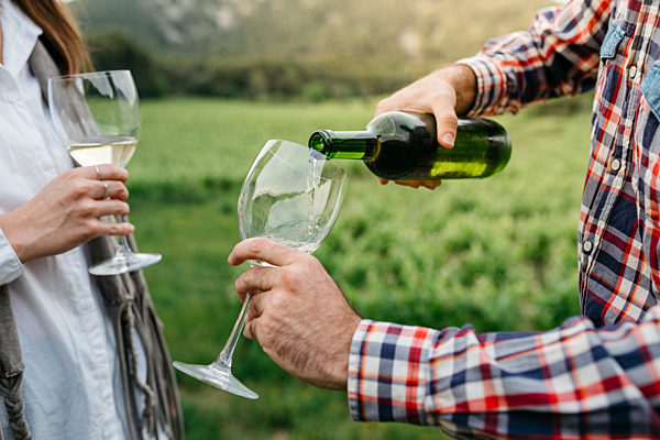 Man serving white wine in glass while standing with woman at vineyard