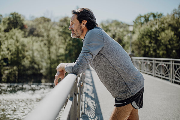Thoughtful mature man looking away while standing by railing on footbridge