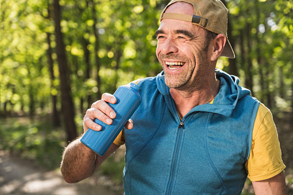 Happy man looking away while holding water bottle at park