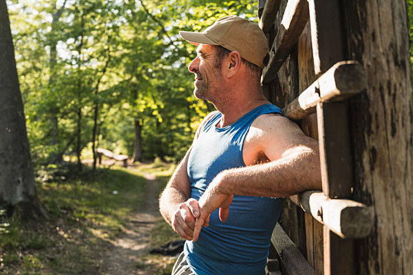 Thoughtful mature man looking away while leaning on wooden ladder at park