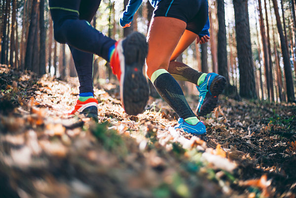Mature couple running on land against trees in woodland