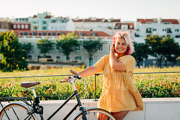 Happy plus size woman with bicycle leaning on park fence