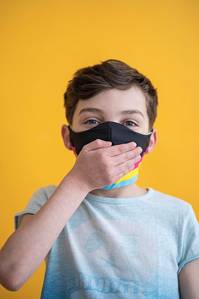 Close-up of boy wearing mask covering mouth with hand against yellow background